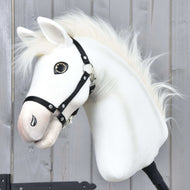 Hobby Horse Nexus s černou ohlávkou od Hobby Horse LarDen, s bílou plyšovou hlavou inspirovanou plemenem Akhal-Teke, knoflíkovým okem a huňatou hřívou, zobrazený na pozadí dřevěné stěny – ideální pro každého nadšence do Hobby Horse Nexus.