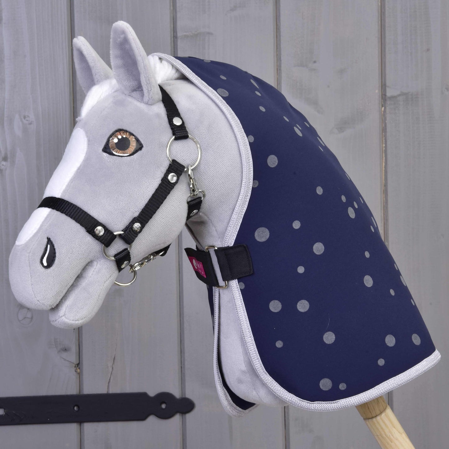 Sivý plyšový Hobby Horse od Hobby Horse LarDen s čiernou uzdečkou a Dekou stajňovou Night Sky, nasadený na drevenej tyči na pozadí svetlej drevenej steny.