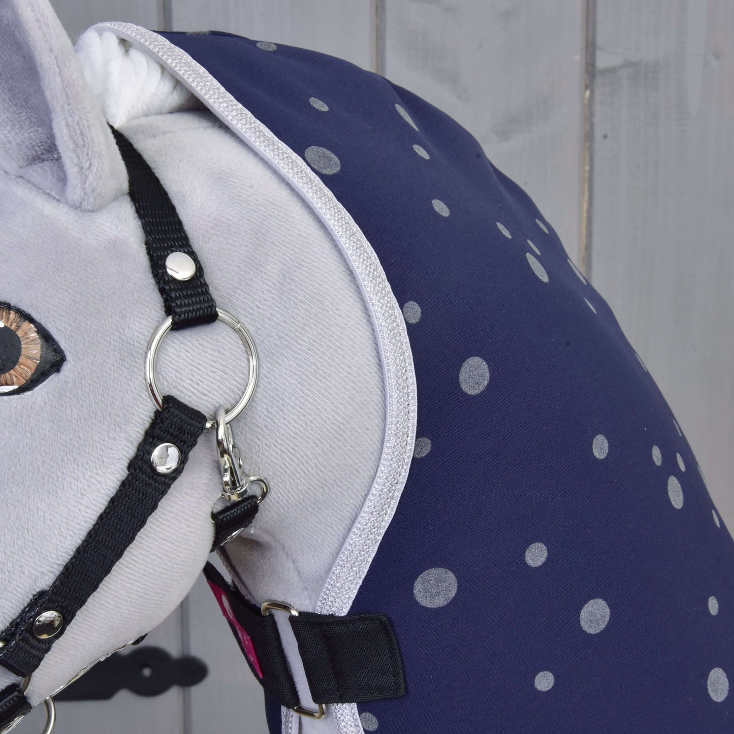 Detail plyšového koňa s Dekou stajňovou Night Sky od Hobby Horse LarDen – tmavomodrou so svetlosivými bodkami – a čiernou ohlávkou, na svetlosivom drevenom pozadí.