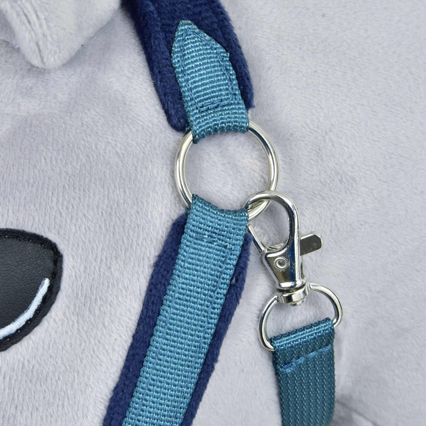 Detail kovovej karabíny a krúžku spájajúcich dva modré nylonové popruhy na mäkkej svetlosivej kožušine, s čiernobielym vyšívaným detailom oka z Hobby Horse LarDen Fur Halter LarDen Blue.
