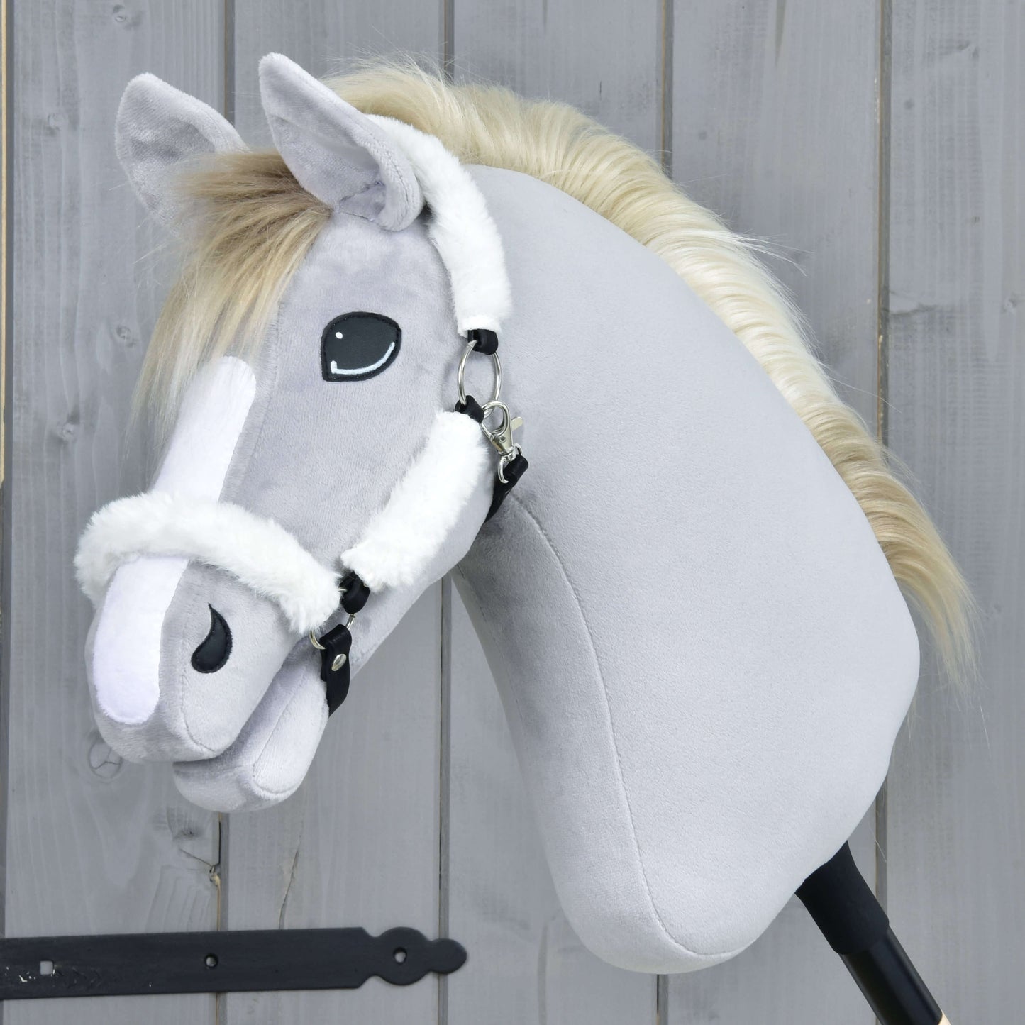 Hobby Horse LarDen Ohlávka s barančekom Teddy Classic na plyšovom Hobby Horse so svetlosivou srsťou, bielou hrivou, bielymi znakmi na hlave a bielou ohlávkou, nasadenom na tyči pred dreveným pozadím.