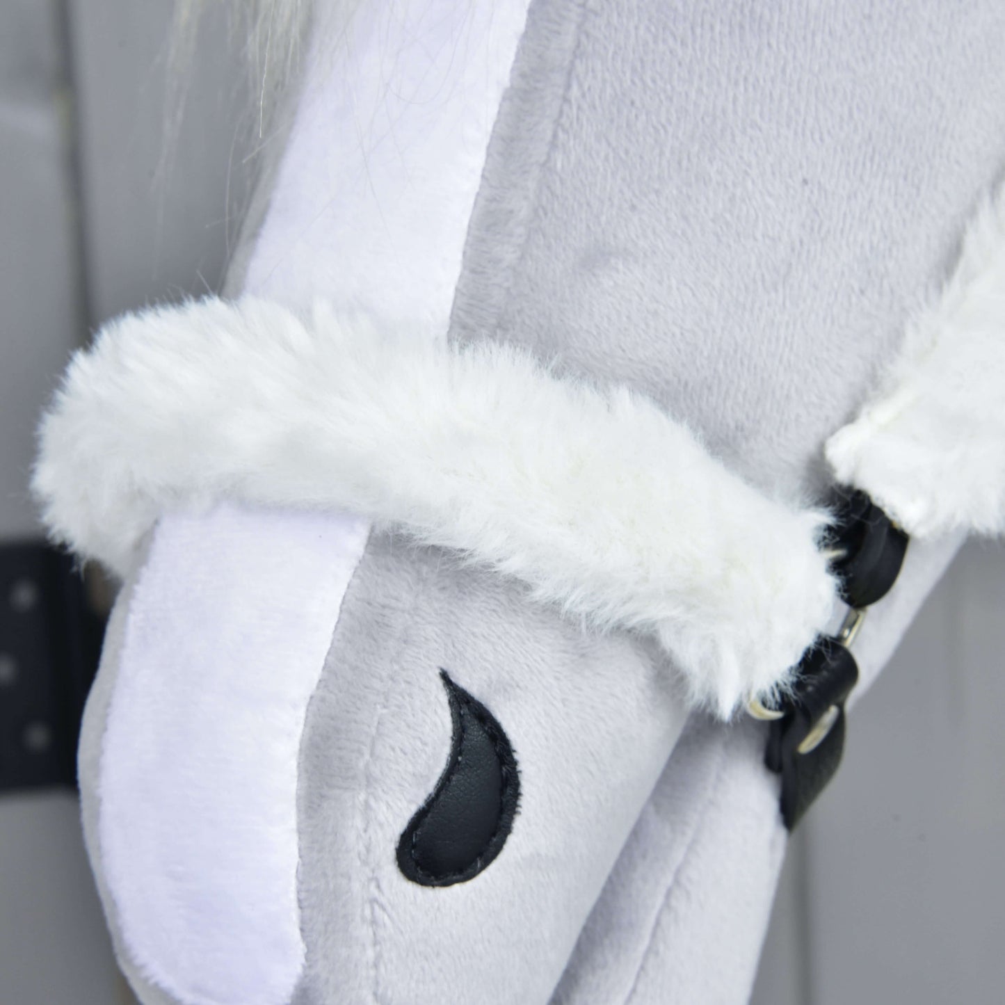 Detail Hobby Horse LarDen Ohlávka s barančekom Teddy Classic na svetlosivom plyšovom Hobby Horse s bielou barančekovou ohlávkou a čiernym vyšitým detailom oka na sivom pozadí.
