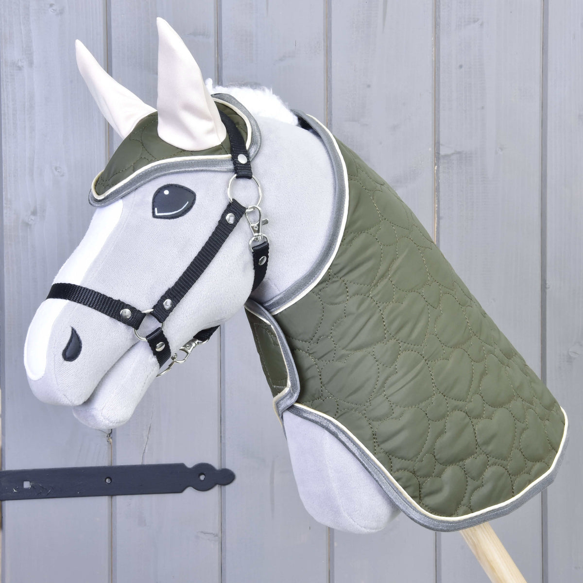 Set Olivetti od Hobby Horse LarDen tvorí sivý Hobby Horse so zelenou prešívanou dekou a uzdečkou, čiernou ohlávkou, bielymi ušami a štýlovými doplnkami, zobrazený pred svetlosivou drevenou stenou.