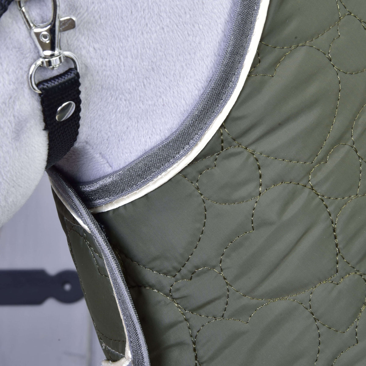 Detail zelenej prešívanej podsedlovej dečky Set Olivetti s bielym lemovaním od Hobby Horse LarDen, s kovovou sponou na čiernom popruhu, pevne nasadenej na svetlosivom koni.