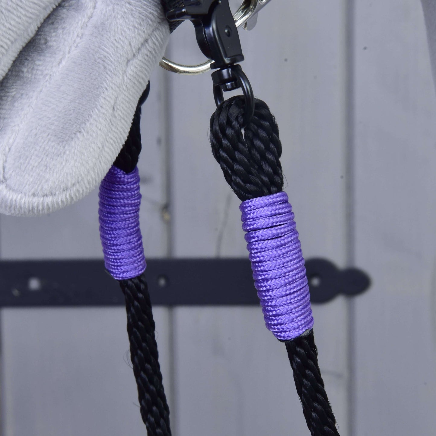 Detail oprát Basic Lila od Hobby Horse LarDen: čierne ručne vyrábané polypropylénové opraty s fialovými akcentmi a striebornou karabínou, na svetlosivom drevenom povrchu s čiernym kovovým pántom.