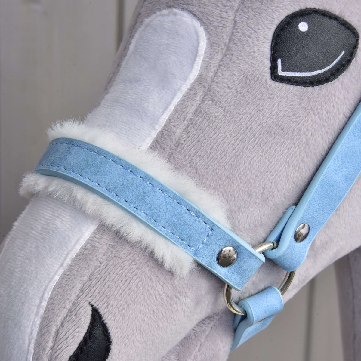 Detail hlavy plyšového hračkárskeho koňa s mäkkou sivou a bielou srsťou, „Ohlávka s barančekom z koženky Pastell Blue“ od Hobby Horse LarDen a vyšívanými čiernobielymi očami.