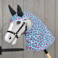 Hobby Horse LarDen Pláštenka Blue Leopard s plyšovým Hobby Horse s bielou tvárou, čiernou uzdečkou a ušami a modrou, ružovou a sivou kapucňou pláštenky so škvrnitým vzorom – všetko na pozadí sivého dreva.