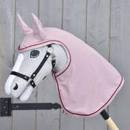 Sivý Hobby Horse LarDen na drevenej tyči má čiernu uzdečku a cez hlavu a krk ružovú Pláštenku Veloria, na pozadí svetlého dreveného plota.