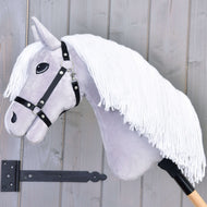 Hobby Horse Popcorn s černou ohlávkou od Hobby Horse LarDen, ze šedé látky, s dlouhou bílou přízovou hřívou a černou ohlávkou na dřevěné tyči, vystavený před světle šedou dřevěnou stěnou.