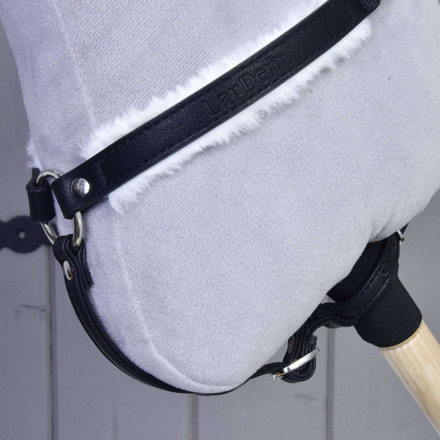 Detail hračky Hobby Horse LarDen s měkkou světle šedou hlavou, černou uzdečkou z umělé kůže a doplňkem Poprsák s beránkem Espresso na dřevěném pozadí.