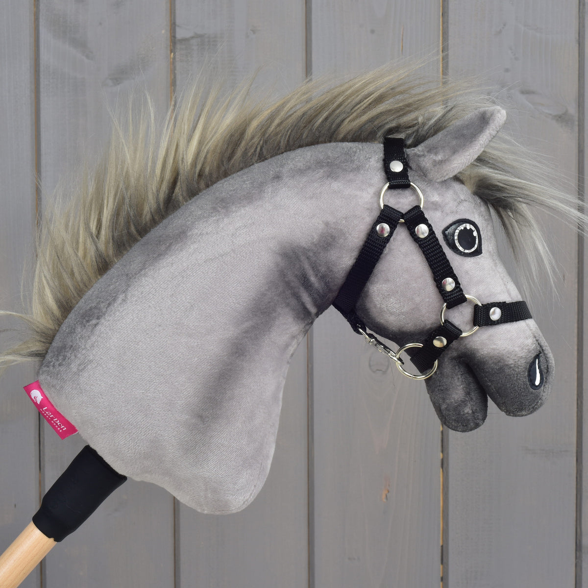 Hobby Horse Prestige s čiernou ohlávkou, veľkosť XS od Hobby Horse LarDen má jemné sivé prevedenie inšpirované anglickým teplokrvníkom a zahŕňa realistickú hrivu a čiernu ohlávku. Je nasadený na drevenej tyči a odfotografovaný na pozadí svetlých drevených panelov, ideálny pre mladých jazdcov snívajúcich o zábave pri parkúrovom skákaní.