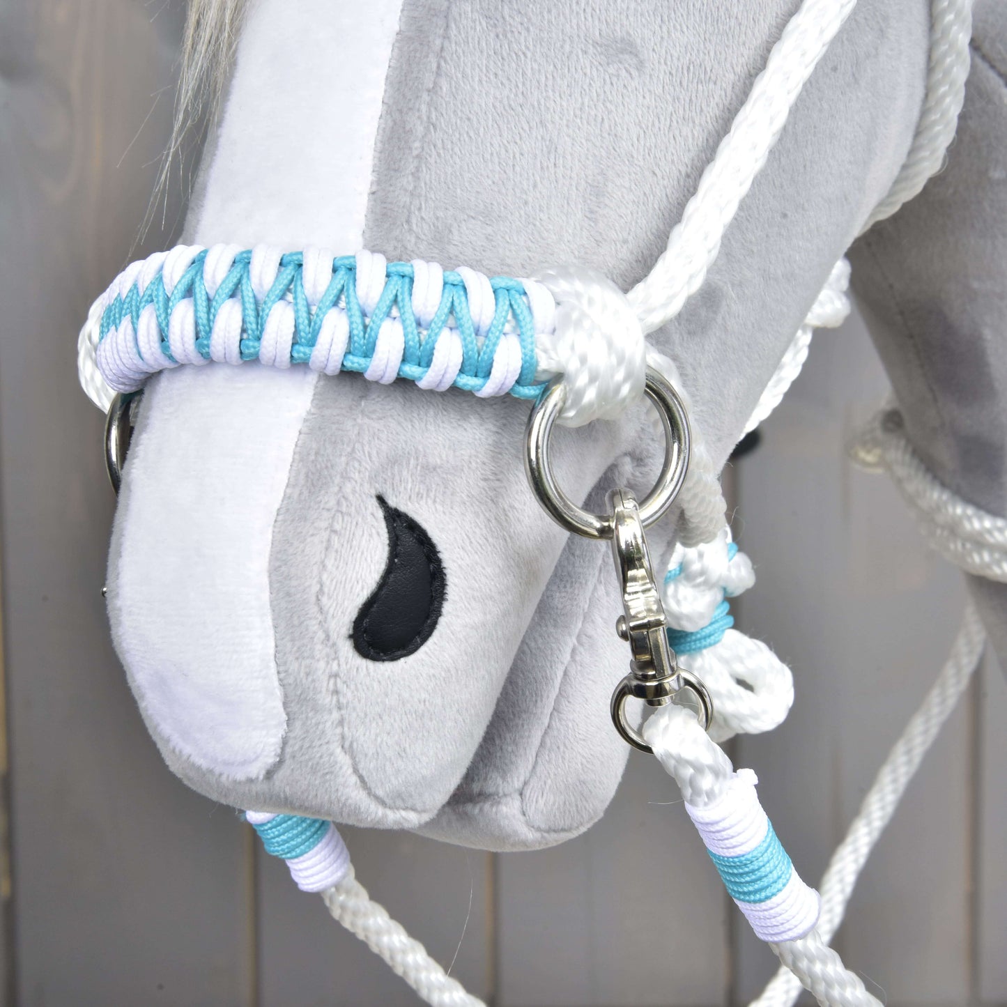 Detail sivej plyšovej hlavy Hobby Horse LarDen s Povrazovým setom White Queen – bielou, modrou a svetlofialovou pletenou ohlávkou a opratami – s čierne vyšitým okom a kovovým krúžkom na postroji.