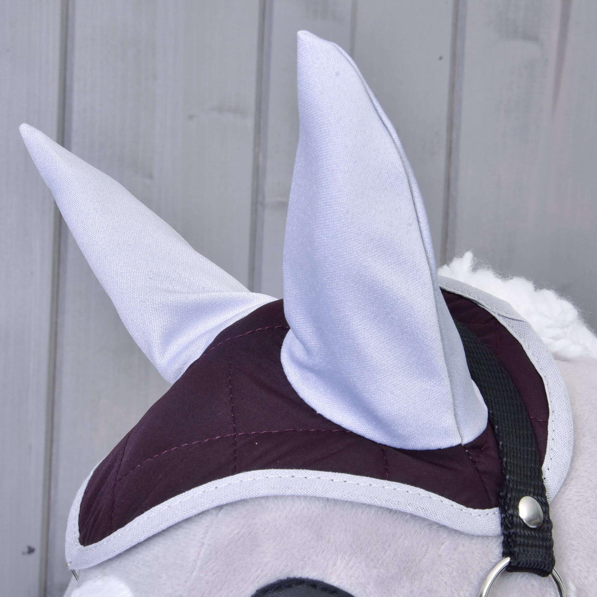 Detail Set Purple od Hobby Horse LarDen: plyšová konská hlava s veľkými sivými uškami, vínovo-sivou prešívanou uzdečkou a náušníkom. V pozadí sú zvislé panely zo svetlosivého dreva.