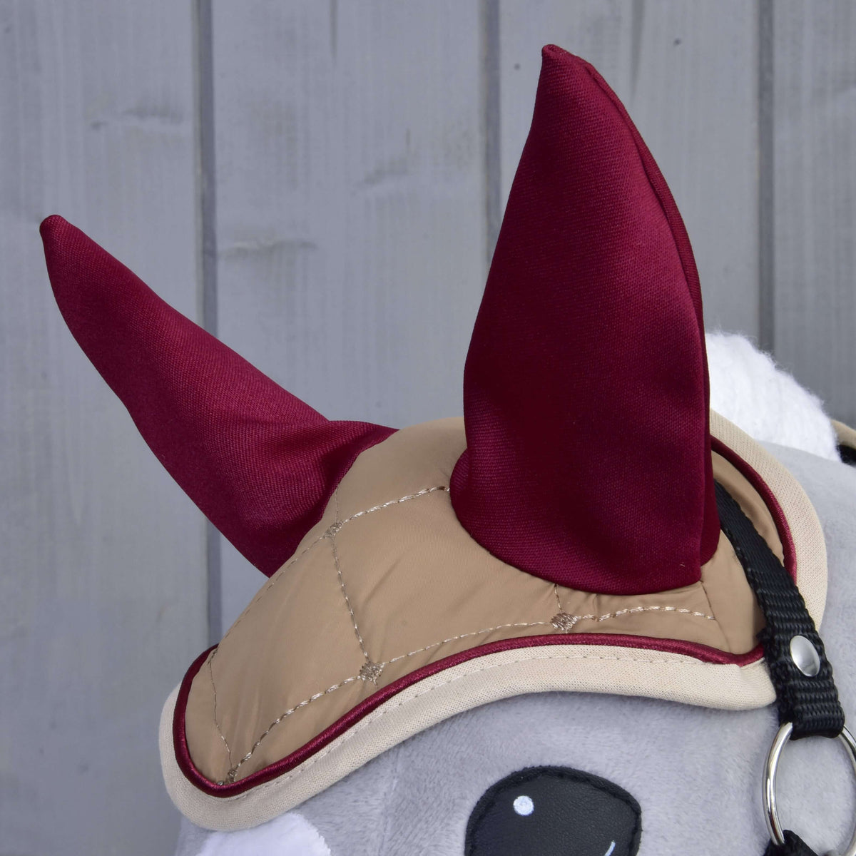 Detail sivej plyšovej hračky Hobby Horse LarDen Set Roma s béžovou uzdečkou a vínovou čabrakou na sivom drevenom pozadí.