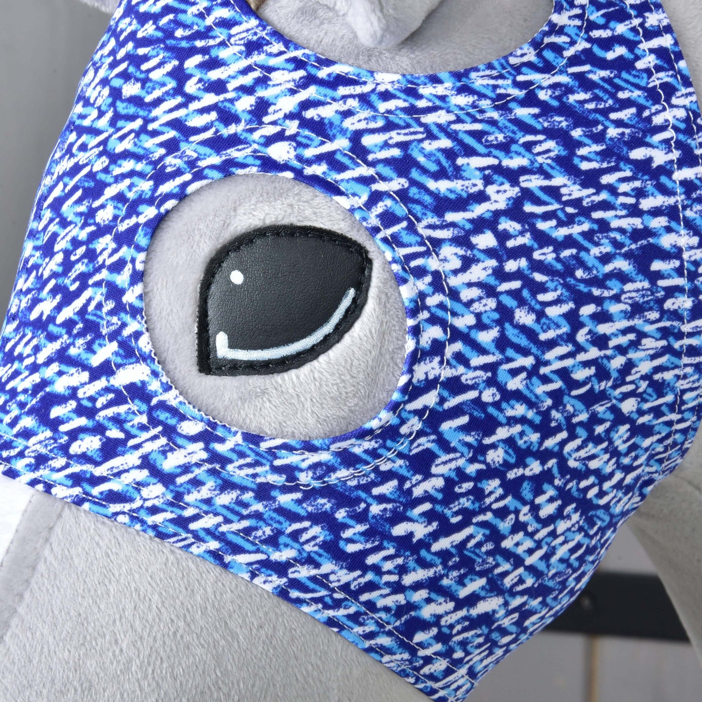 Detail plyšovej hračky zo sivej látky s veľkým vyšívaným okom, ktorá má na sebe Hobby Horse LarDen „Maska bez uší See“, modrobiely prateľný poťah s kruhovým otvorom pre lepšiu ochranu Hobby Horse.