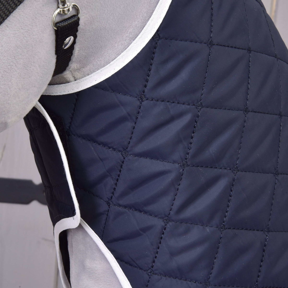 Detail svetlosivého psa v prešívanom tmavomodrom kabátiku Set Monte od Hobby Horse LarDen s bielym lemovaním, kosoštvorcovým vzorom a čiernym pásikom s kovovou prackou pre štýlový vzhľad.