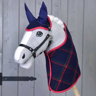 Hobby Horse LarDen „Set Tartan“ s plyšovým Hobby Horse so sivou tvárou, čiernou uzdečkou, modrými ušami a tmavomodrou károvanou dekou s červeným lemom, pred sivou drevenou stenou.