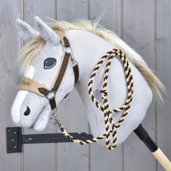 Set LarDen Exclusive Braun od Hobby Horse LarDen, plyšový sivý Hobby Horse s bielou hrivou, hnedou uzdečkou, fleecovým nánosníkom a pletenými povrazovými opratami na drevenej tyči, na pozadí sivej drevenej steny.