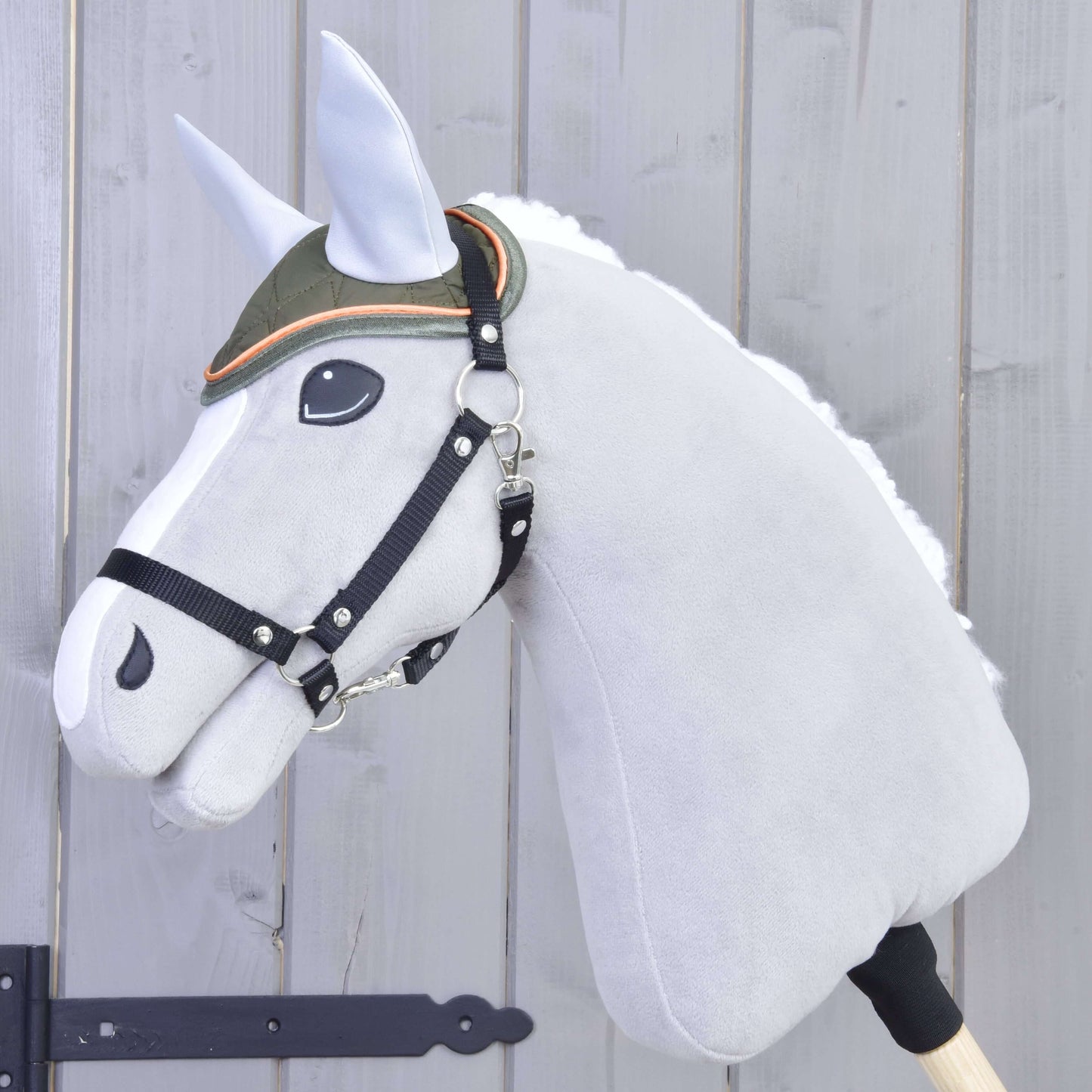 Plyšový Hobby Horse LarDen na tyči s bielou hrivou, sivou tvárou, čiernou uzdečkou a vyšívaným okom má nasadenú čabraku Sport – zelenú čabraku s oranžovým lemovaním – na svetlom drevenom pozadí.