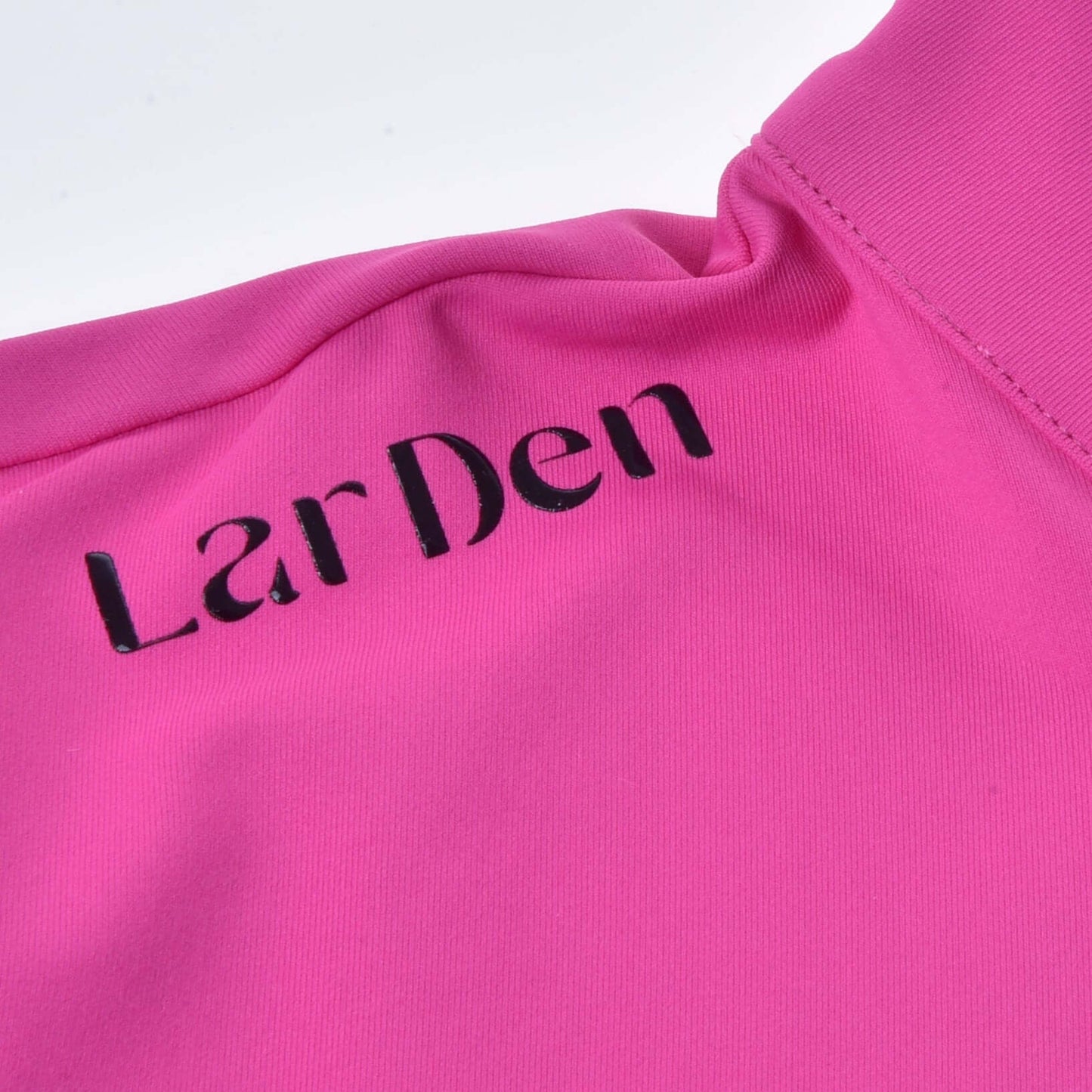 Detail Športového trička LarDen Pink od Hobby Horse LarDen s krátkymi rukávmi, hladkou spandexovou látkou, viditeľným prešívaním a textúrou a čiernym nápisom „LarDen“ vytlačeným na žiarivo ružovom materiáli.