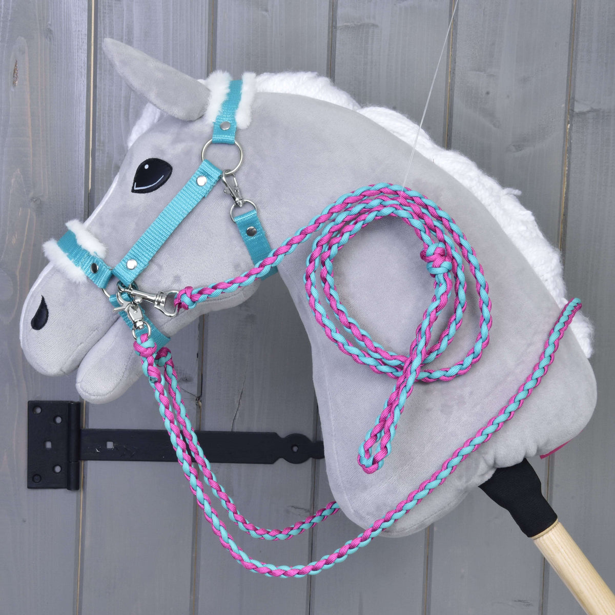 Set Perfect Combination Turquoise od Hobby Horse LarDen, plyšový sivý Hobby Horse s bielou hrivou, tyrkysovou uzdečkou, ohlávkou s kožušinovým polstrovaním a ružovo-modrými povrazovými oprátami, visí pred sivou drevenou stenou.
