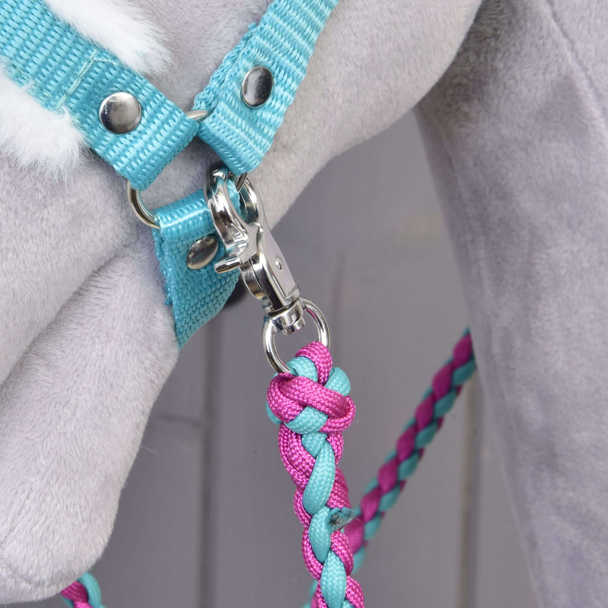 Detailný záber na Set Perfect Combination Turquoise od Hobby Horse LarDen s pleteným ružovo-modrým vodidlom pripnutým k tyrkysovej ohlávke s kožušinovým polstrovaním na svetlosivom plyšovom koni – ideálny pre fanúšikov doplnkov pre Hobby Horse.