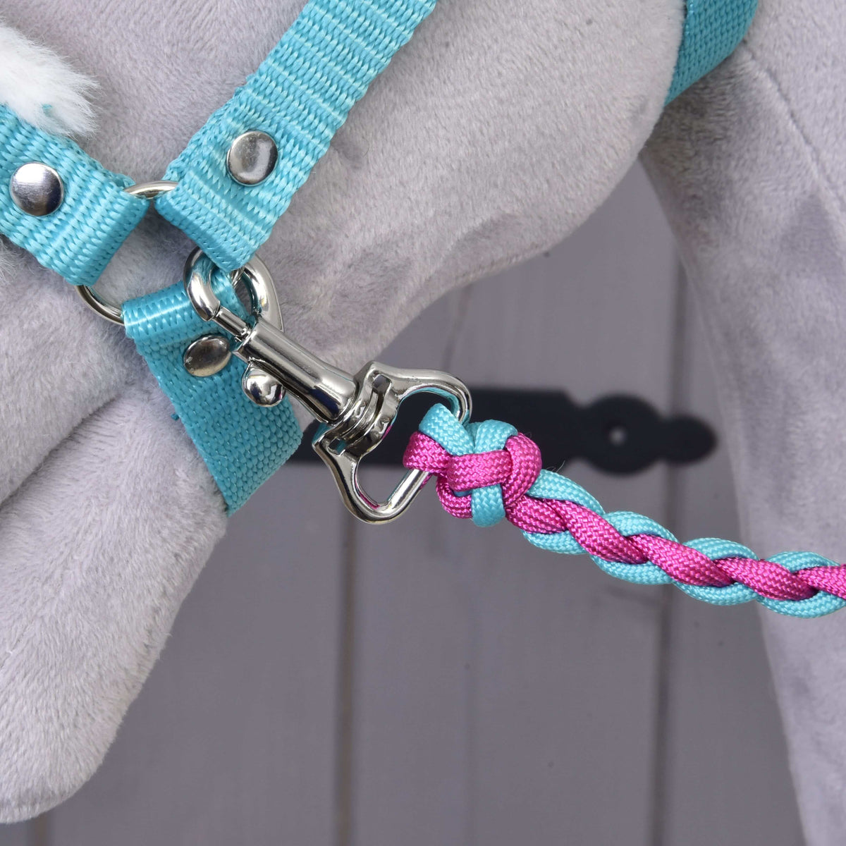 Detailný záber na vodidlo Set Perfect Combination Turquoise od Hobby Horse LarDen, pletené v modrej a ružovej farbe a pripnuté k svetlomodrému postroju na sivom plyšovom zvierati – ideálny pre doplnky pre Hobby Horse. Rozmazané pozadie.