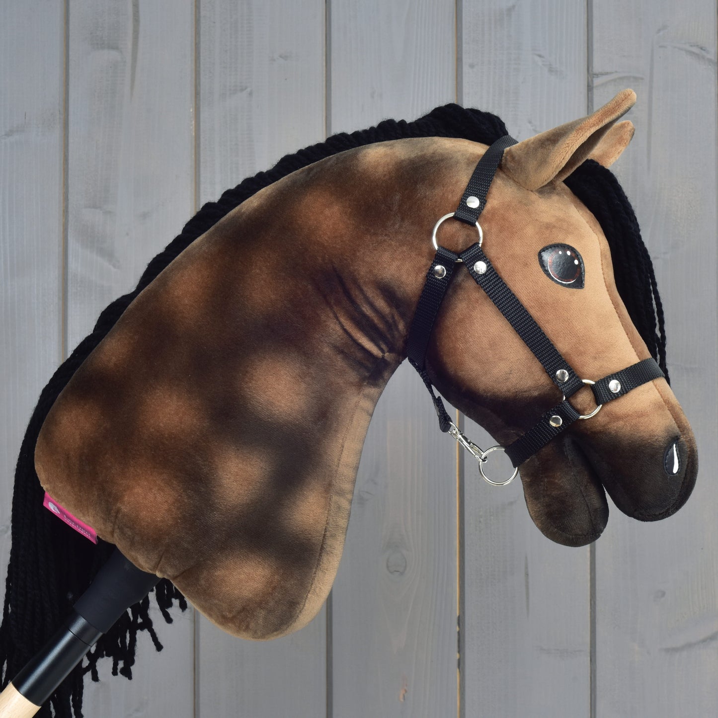 Hobby Horse Stormy s čiernou ohlávkou od Hobby Horse LarDen, plyšový šimľový Hobby Horse s hnedočiernou hrivou, pred dreveným panelovým pozadím.