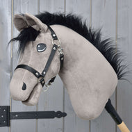 Hobby Horse Thor s černou ohlávkou od Hobby Horse LarDen, plyšový hanoverský hřebec Hobby Horse s černou hřívou, černou ohlávkou a vyšívanýma očima, na dřevěné tyči před světle šedou dřevěnou stěnou.