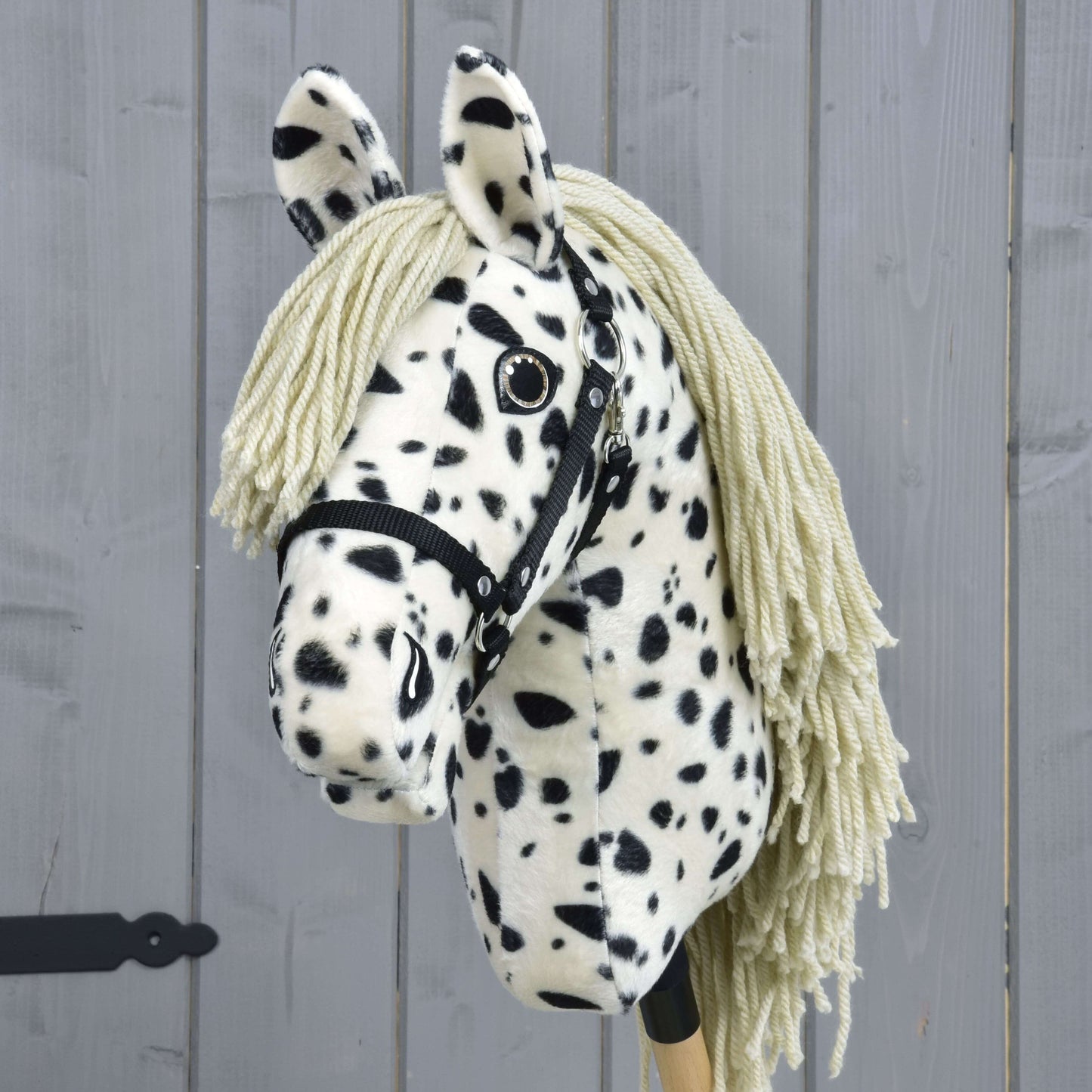 Hobby Horse Lord Valentine s čiernou ohlávkou od Hobby Horse LarDen, s čiernobielou strakatou srsťou, priadzovou hrivou a čiernou ohlávkou, na pozadí sivého dreva.