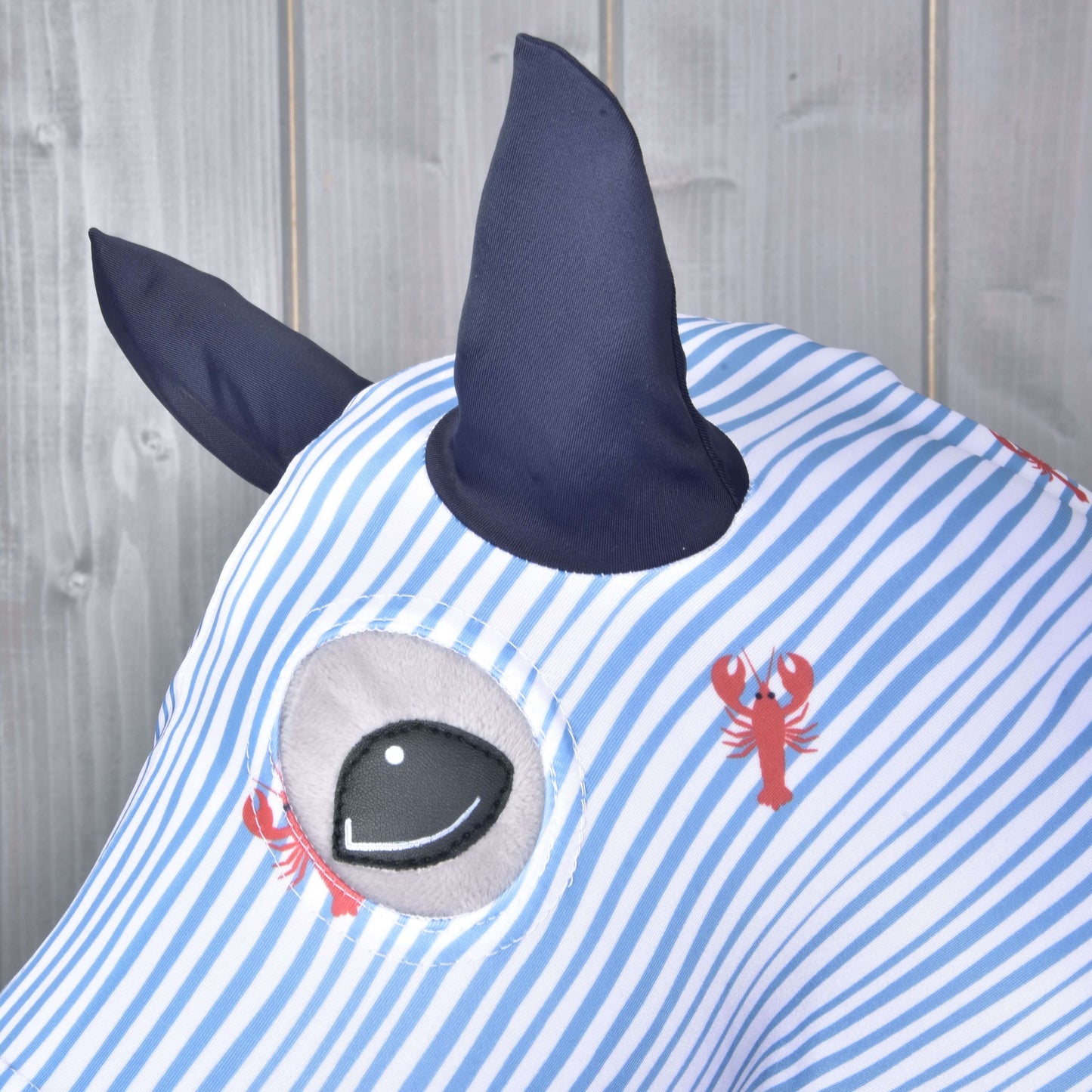 Detailný záber na Hobby Horse ochranný oblek Andromeda (Lycra) od Hobby Horse LarDen ukazuje modro-biele pruhy, mäkkú látku PES a Lycra, tmavomodré rohy, veľké kreslené oko a červené potlače homárov – ideálny pre hravú ochranu Hobby Horse.