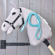 Hobby Horse - vodítko Atlantis od Hobby Horse LarDen s šedou plyšovou hlavou, černou uzdečkou a modrým provazovým vodítkem, upevněné na dřevěné tyči a zobrazené před svislými dřevěnými prkny.