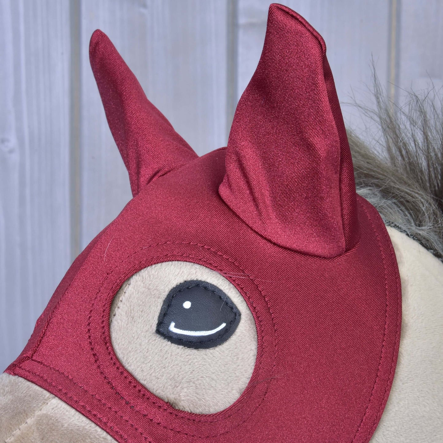 Detail plyšovej hračky Hobby Horse LarDen s Maska Barn Red, so špicatými ušami a sivou hrivou, na svetlom drevenom pozadí.