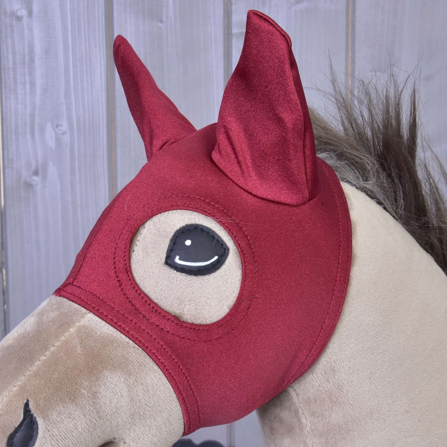 Béžový plyšový Hobby Horse od Hobby Horse LarDen s Maska Barn Red, so špicatými ušami a veľkými kreslenými otvormi na oči, na pozadí drevených panelov.