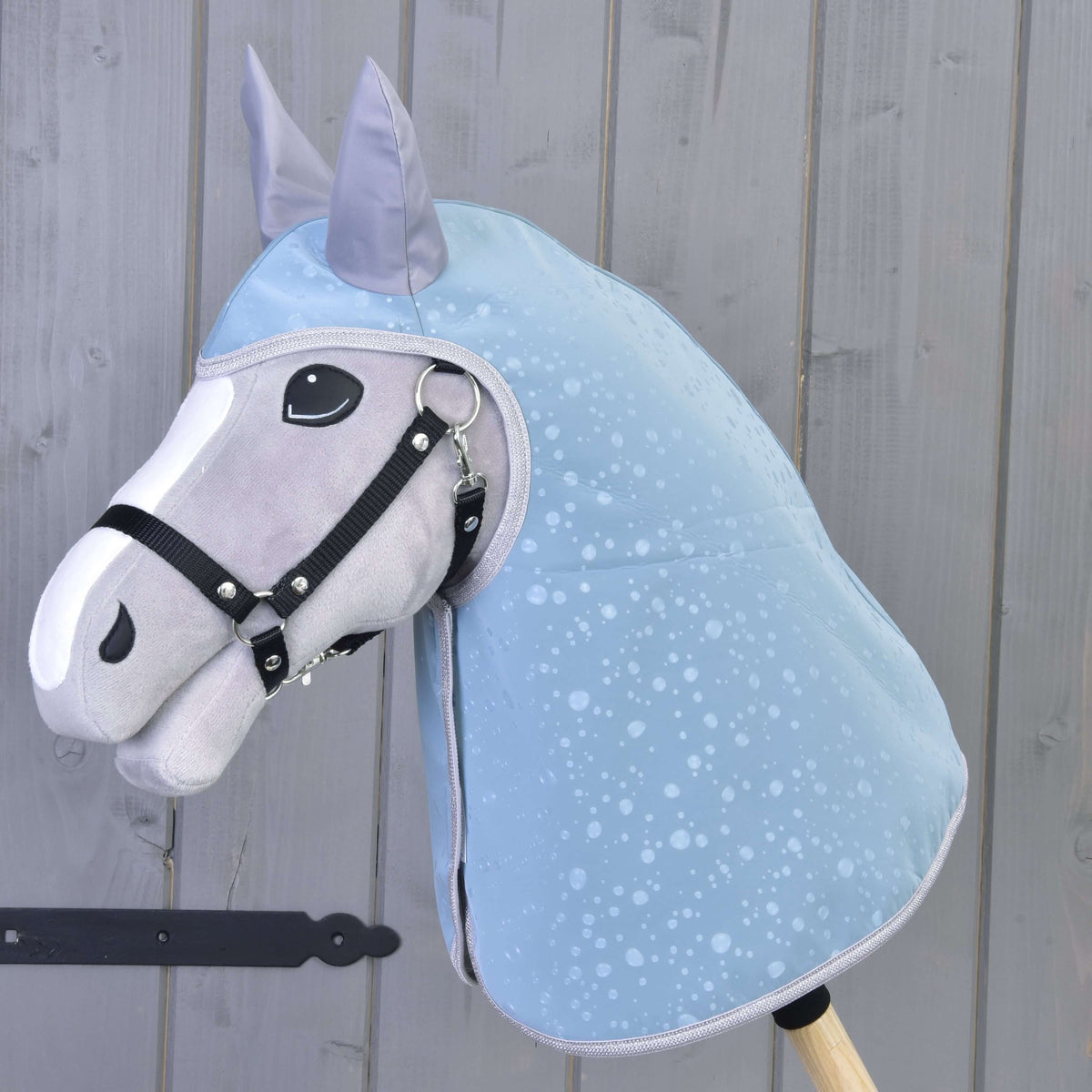 Pláštenka Blue Drops od Hobby Horse LarDen, zobrazená na sivo-bielom Hobby Horse s čiernou uzdečkou pred svetlým dreveným plotom — ideálny doplnok pre tvoj Hobby Horse do každého počasia.