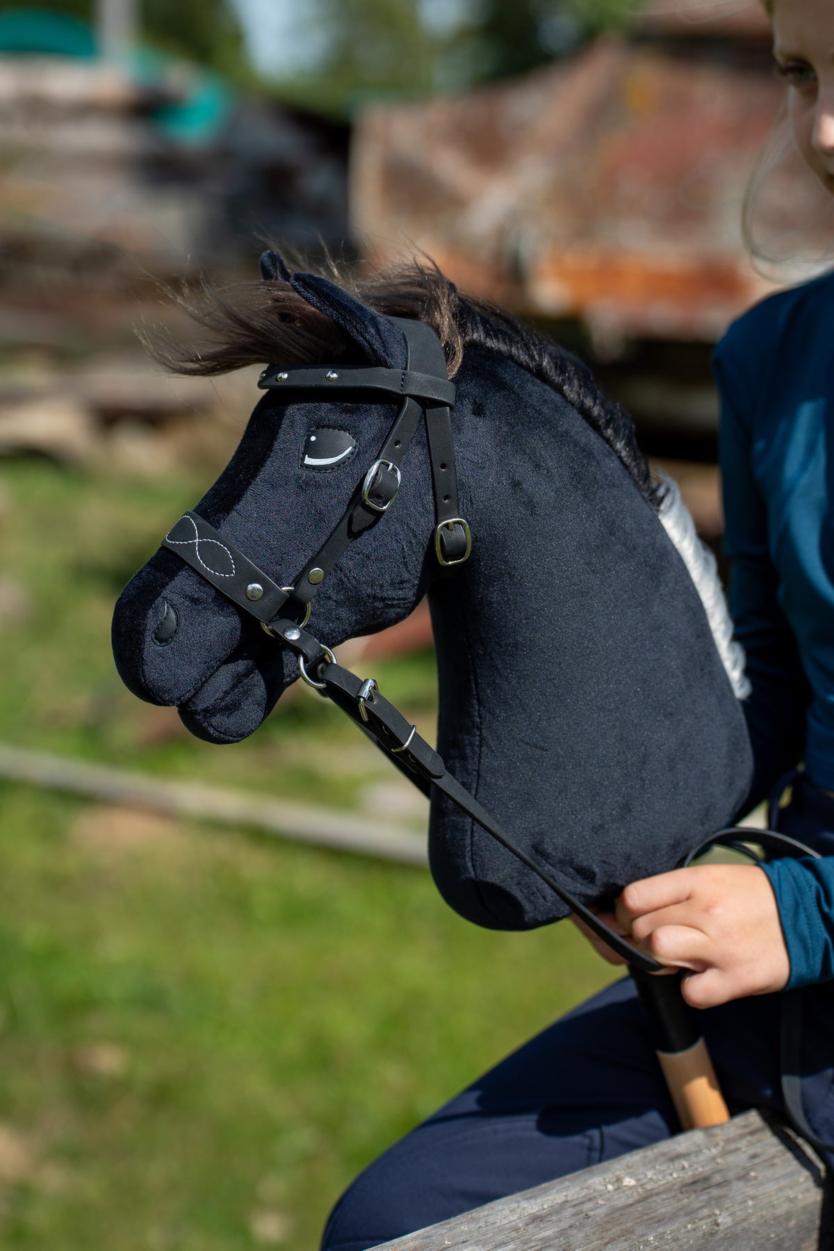 Hlava Hobby Horse Bond s čiernou ohlávkou od LarDen pred rozmazaným dvorom, čierny plyš, tmavohnedá priadzová hriva a čierne remene so striebornými prackami, s ozdobnou bezudidlovou uzdečkou