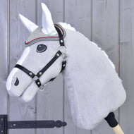 Detail šedého plyšového Hobby Horse od Hobby Horse LarDen s uzdečkou, ozdobným čelenkovým řemínkem a čabrakou Silver Eleganza pro ochranu před hmyzem, na pozadí dřevěného plotu.