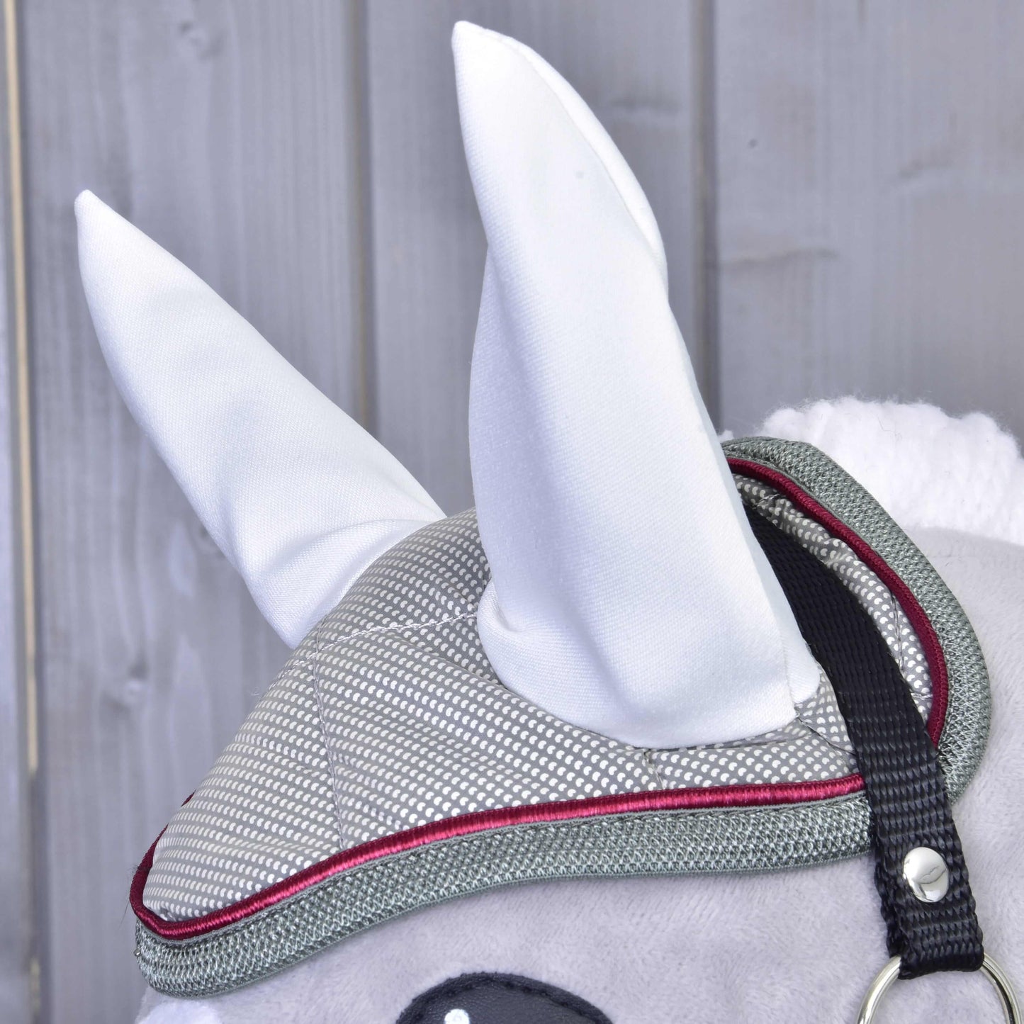 Detail sivého Hobby Horse od Hobby Horse LarDen s čabrakou Silver Eleganza a sivo-červenou uzdečkou, s veľkými bielymi ušami, na pozadí drevených panelov.