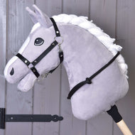 Nákrčník čierny od Hobby Horse LarDen na sivom plyšovom Hobby Horse s bielou hrivou na drevenej tyči, s čiernou uzdečkou, opratami a ručne vyrobeným cordeom, pred sivou drevenou stenou.