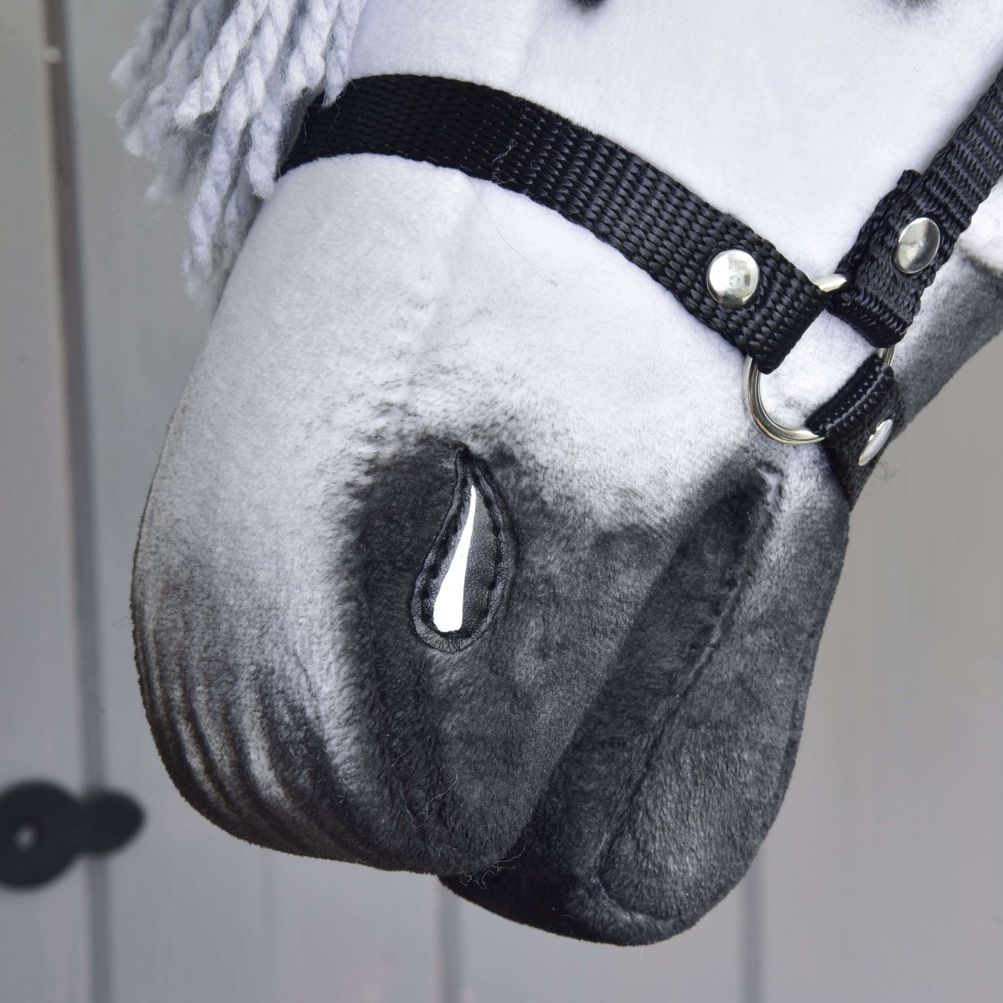 Detail ručne vyrobeného Hobby Horse Chantal s čiernou ohlávkou od Hobby Horse LarDen, s bielo-sivým sfarbením, maľovaným detailom slzy, priadzovou hrivou a neutrálnym pozadím.