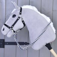 Pletené otěže Cremo/Blue od Hobby Horse LarDen na šedém plyšovém Hobby Horse s bílou hřívou, černou uzdečkou, ručně vyráběnými otěžemi, stříbrným kováním a modrobílým pleteným vodítkem, nasazeném na dřevěné tyči před šedou dřevěnou stěnou.