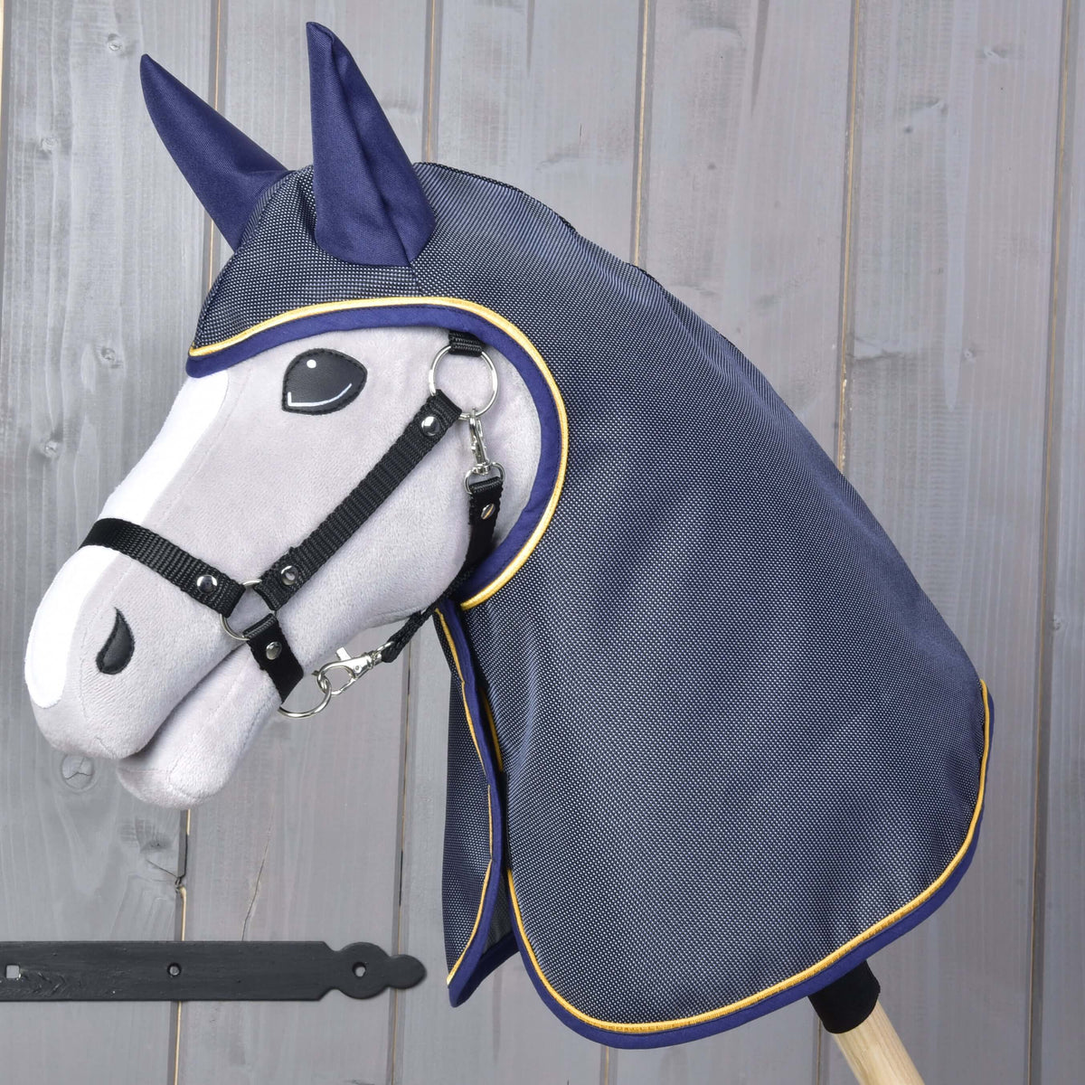 Pláštenka Crone od Hobby Horse LarDen so sivou plyšovou hlavou Hobby Horse na tyči, čiernou uzdečkou a tmavomodrou pláštenkou so žltým lemovaním, zobrazená na drevenom pozadí.
