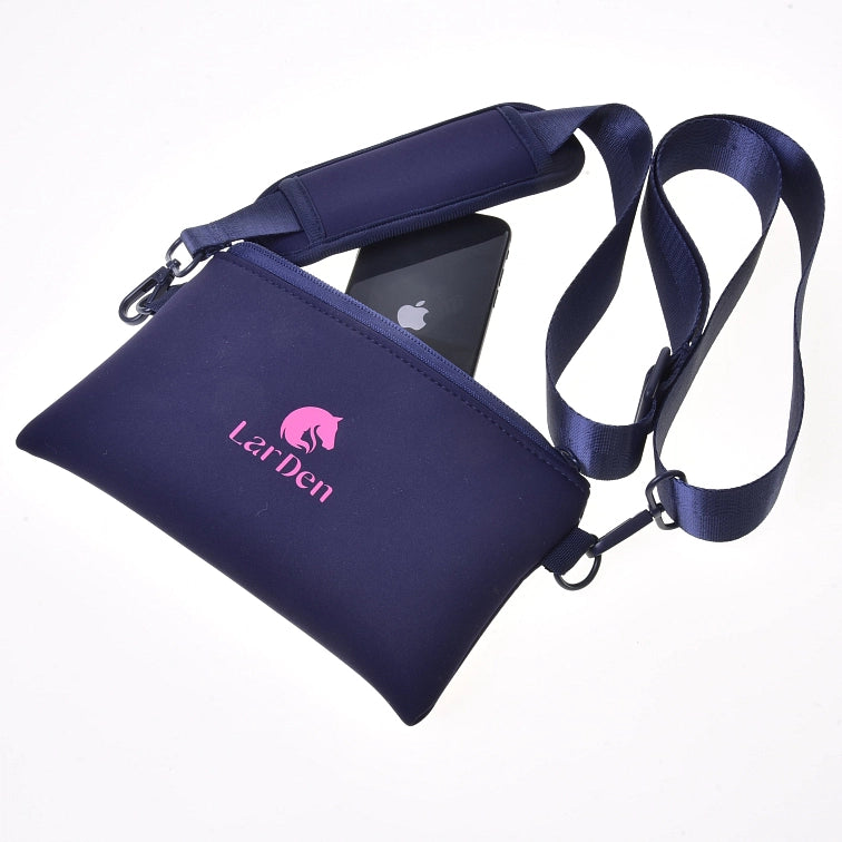 Tmavomodrá crossbody taška LarDen s ružovým logom, zobrazená s nastaviteľným popruhom a čiernym smartfónom čiastočne zasunutým v priehradke na zips – ideálna na prenášanie nevyhnutností na tvoju ďalšiu akciu Hobby Horsing – na bielom pozadí.