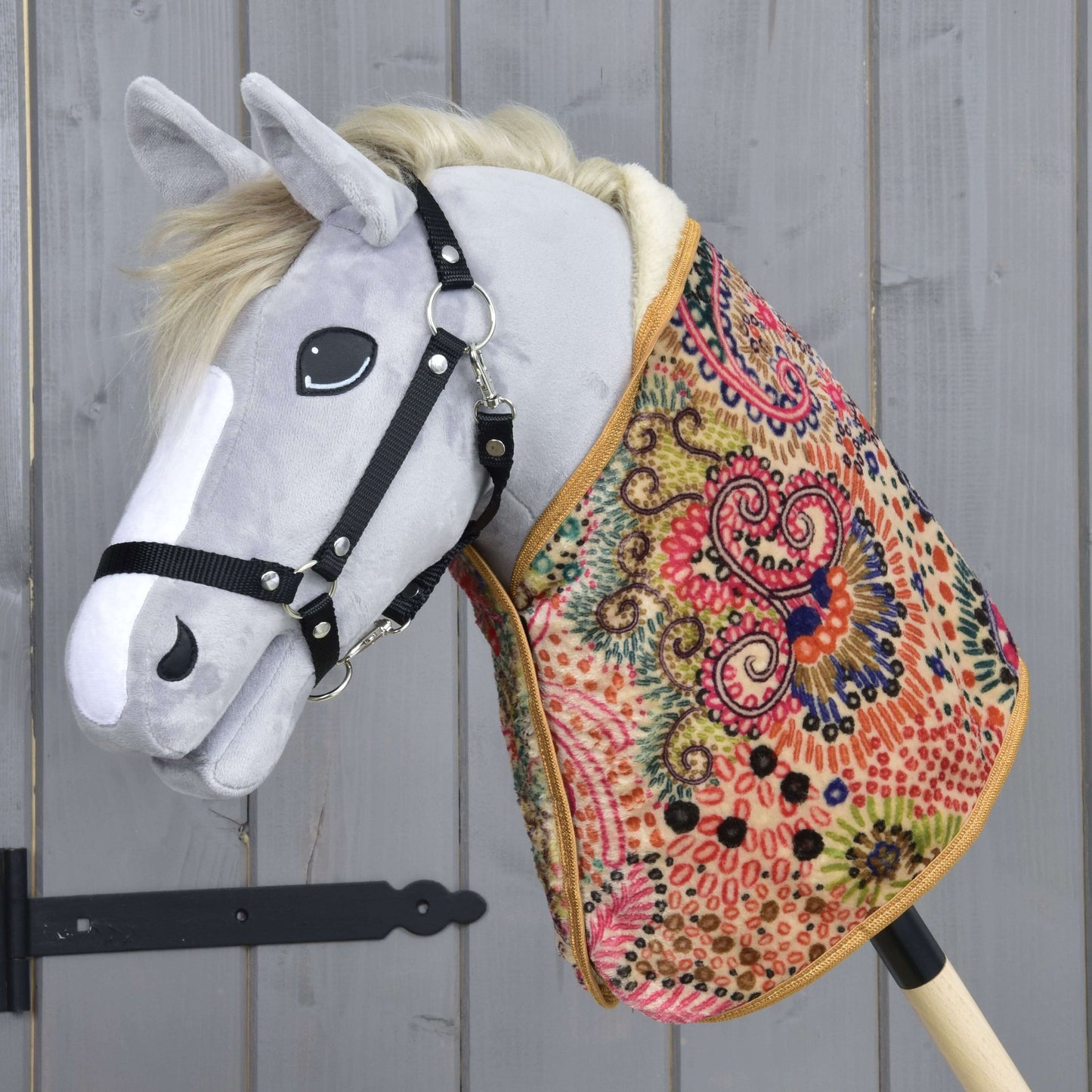 Hobby Horse LarDen „Deka Jungle“ je plyšový Hobby Horse so sivou hlavou, čiernou uzdečkou a farebným dekovým telom — ideálny pre imaginatívnu hru alebo raný tréning s koňom — zobrazený pred pozadím z drevených panelov.