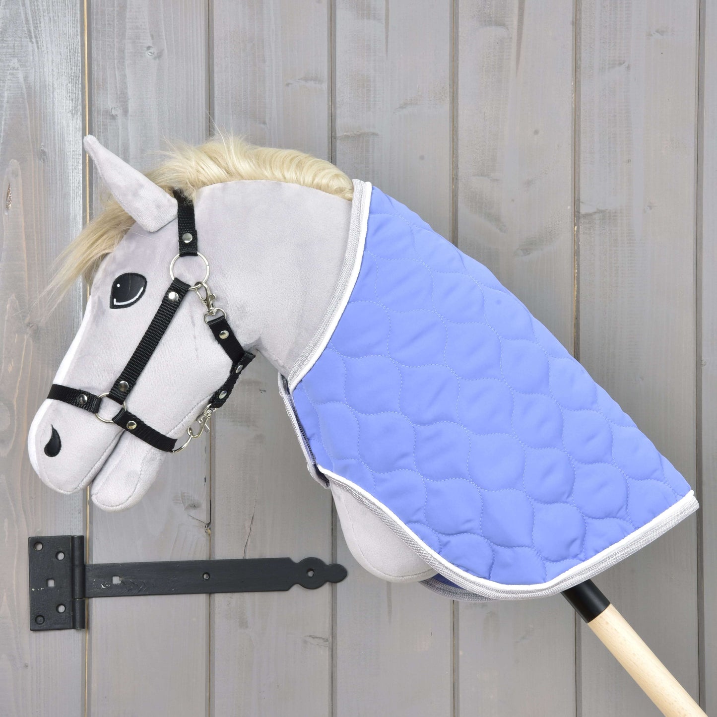 Sivý Hobby Horse s čiernou uzdečkou a dekou Hobby Horse LarDen "Blanket Light Violett" je nasadený na tyči a zobrazený pred svetlou drevenou stenou.