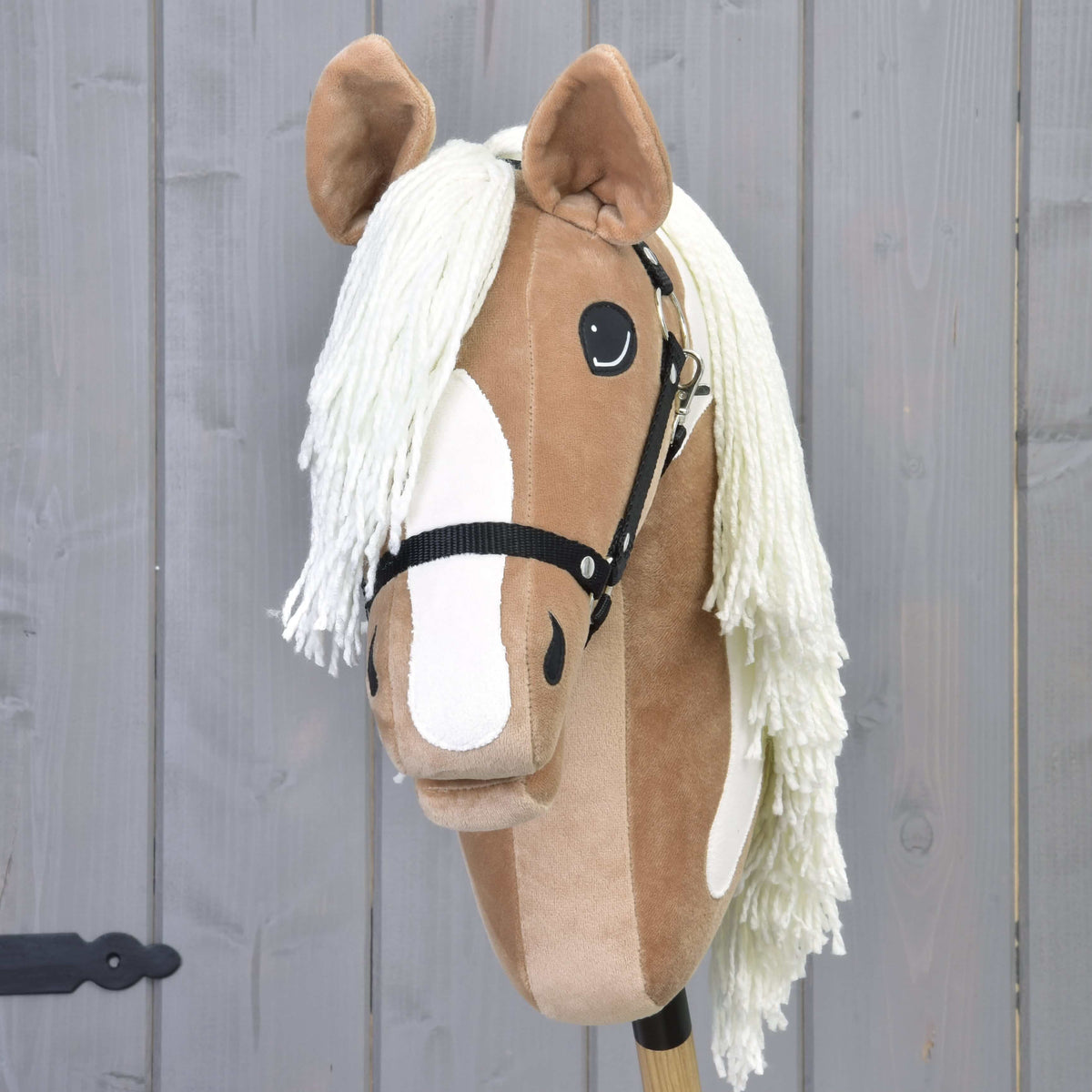 Hobby Horse Fury s čiernou ohlávkou od Hobby Horse LarDen má svetlohnedú a bielu tvár, čiernu ohlávku a dlhú bielu hrivu, pripomína American Paint Horse a je umiestnený pred sivým dreveným pozadím. Ideálny pre nápadité dobrodružstvá.