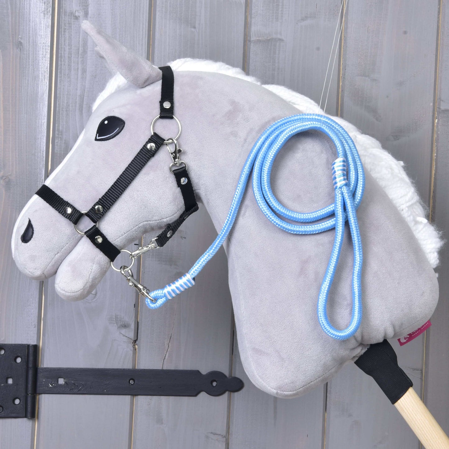 Hobby Horse - vodítko Heaven od Hobby Horse LarDen, šedý plyšový Hobby Horse s bílou hřívou, černou uzdečkou, modrobílým vodítkem a tyčí, zobrazený před světlou dřevěnou stěnou, ideální pro hru na vedení nebo lonžování.