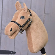 The Build your horse by related_to_12441055625556, a plush caramel hobby horse with black halter and chocolate yarn mane, featuring stitched eyes and nose, is set against a wooden wall.