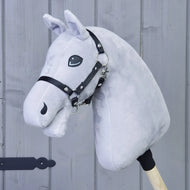 A “Build your horse” hobby horse from related_to_12441055625556, featuring a light grey body, striking black-grey-white mane, and a black bridle attached to a wooden stick, is displayed against a gray wooden wall background.