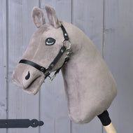 The "Build your horse" plush taupe hobby horse by related_to_12441055625556 features a black bridle and white yarn mane on a wooden stick, displayed before a gray wood panel background.